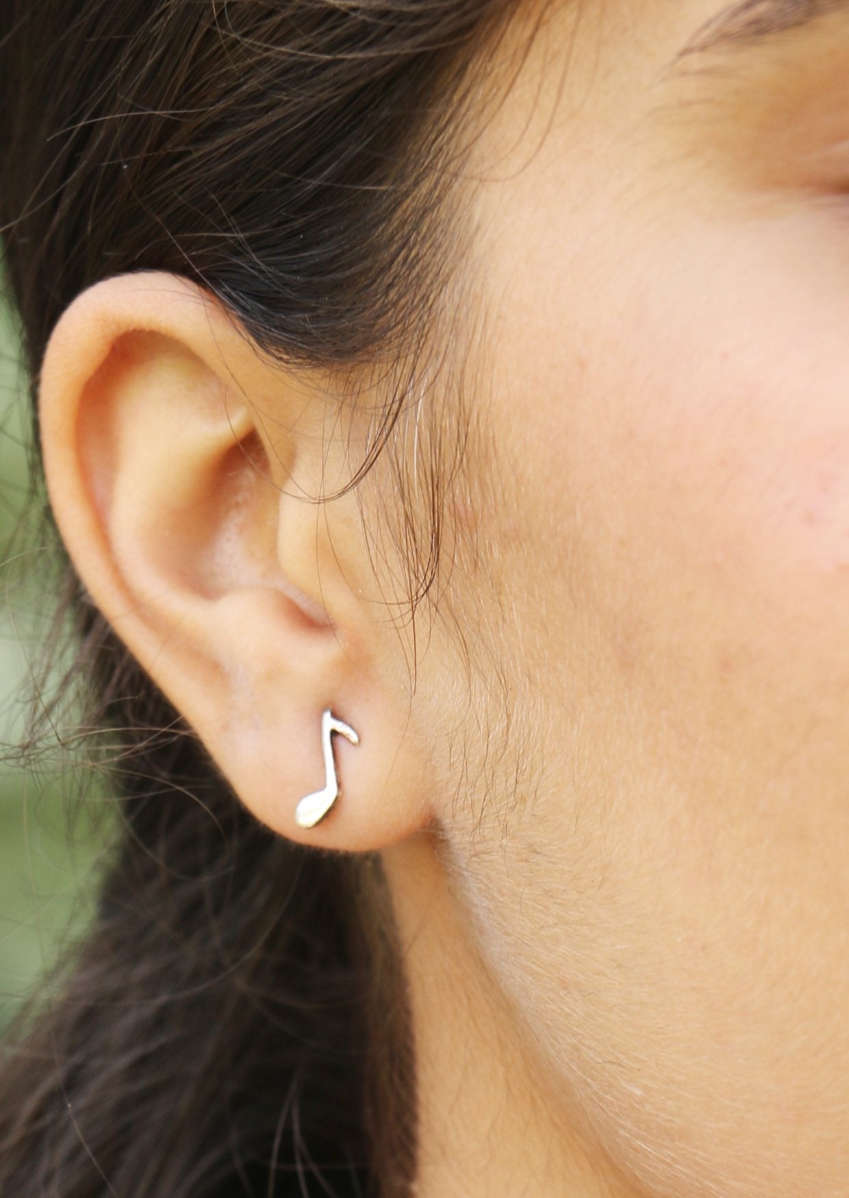 Close-up of an ear wearing a silver music note earring with secure butterfly backs