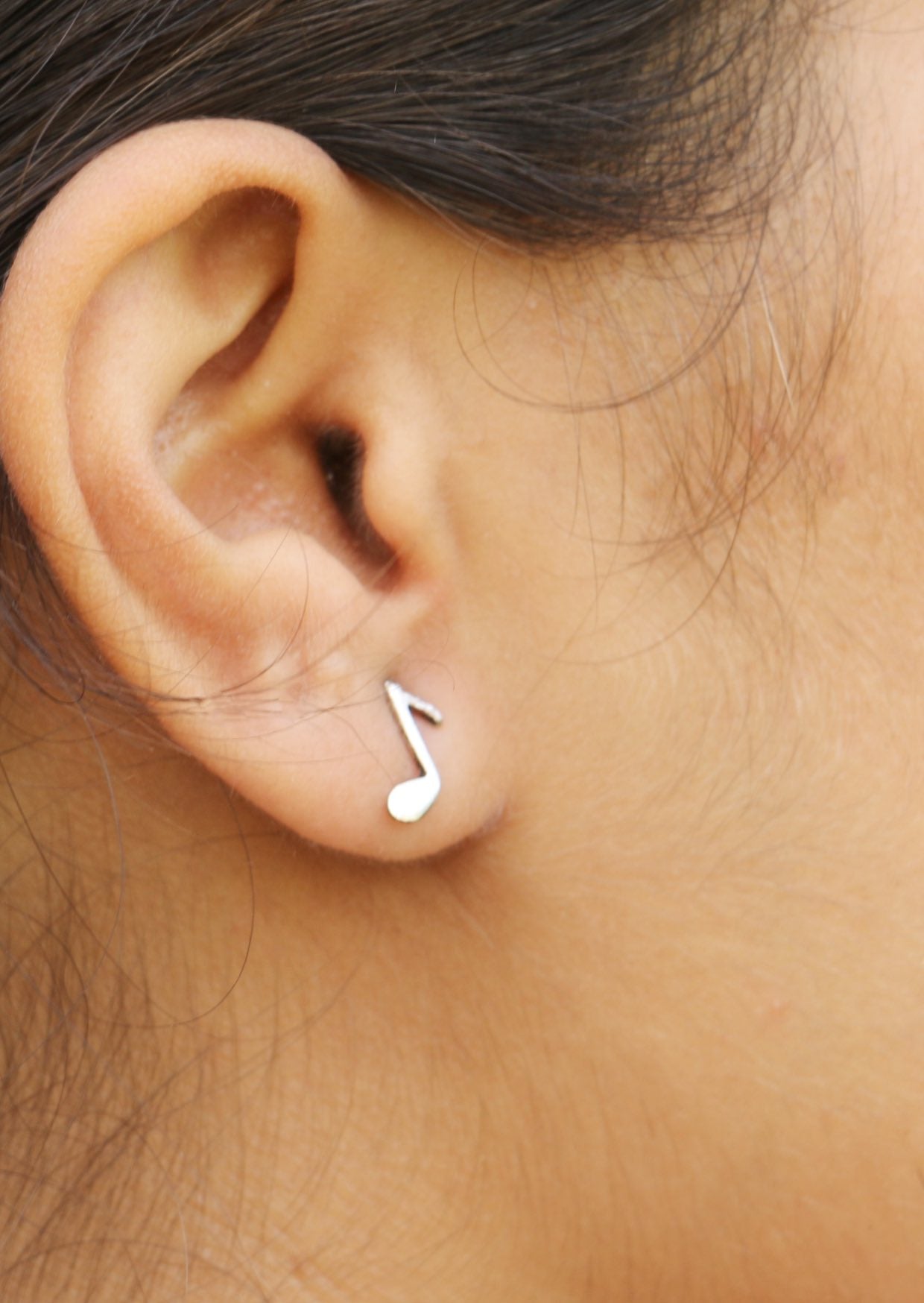 Close-up of an ear wearing a sterling silver quaver studs, music note earring with butterfly backs 
