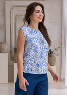 Woman wearing a white based blue floral, loose fit cotton top in an indoor setting.