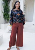 Woman wearing a protea patterned top and red cotton pants standing in a bright outdoor setting.