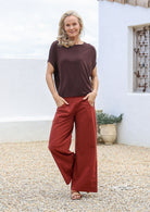 Woman wearing 100% cotton high waisted wide leg pants in rust shade with pockets, side zipper and wide flat waistband.