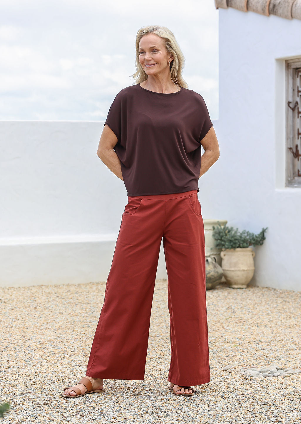 Woman is posing in rust coloured wide leg cotton pants with wide flat waistband, pockets and a side zipper 