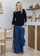 Woman wearing blue cotton wide leg pants paired with a black top, with hand in pocket