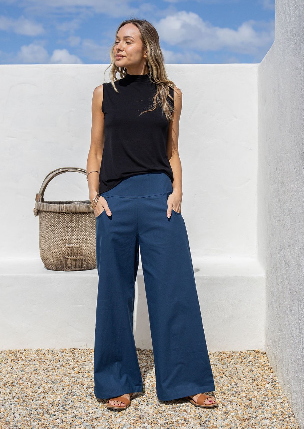 Woman wearing blue cotton wide leg pants with a wide waistband, side zipper, and pockets, standing against a white wall