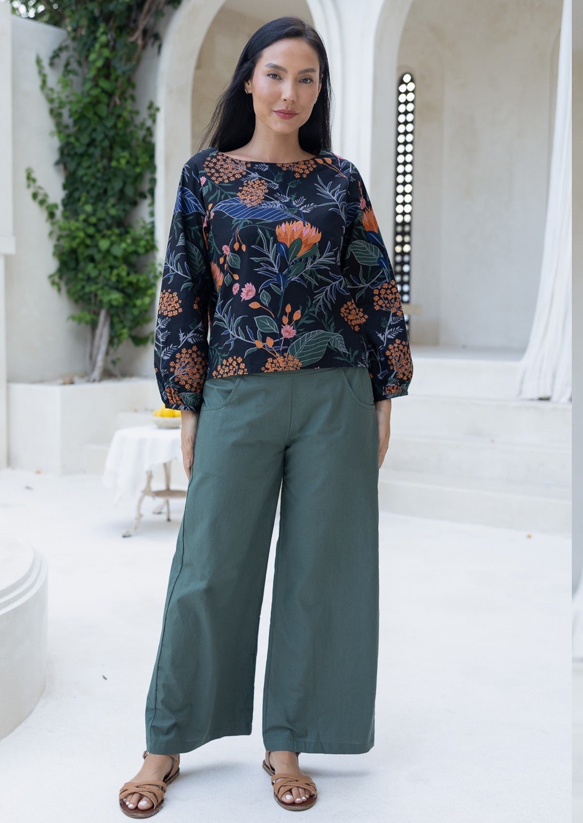 Woman wearing a black based floral top and green pants with wide legs and sandals