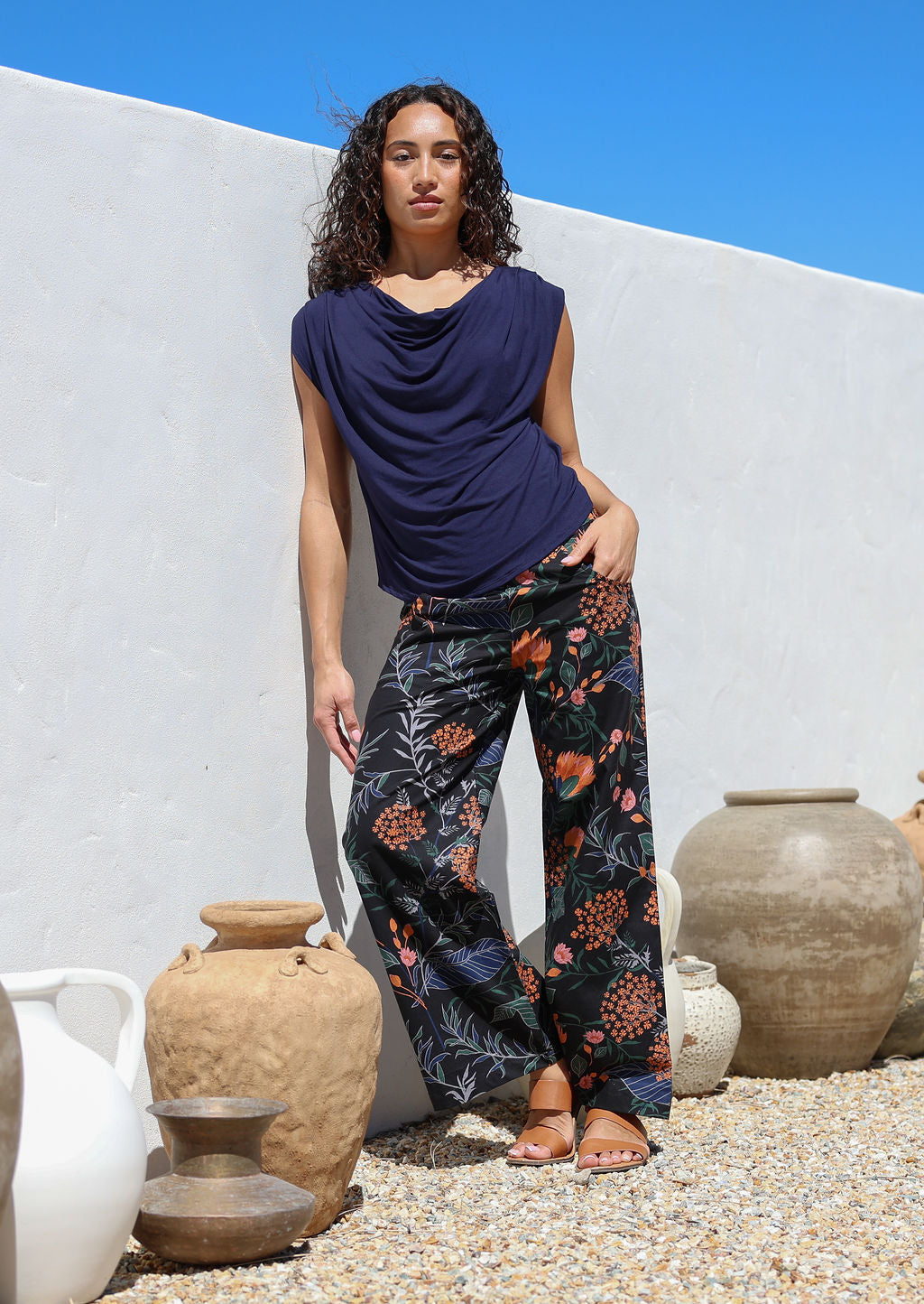 Model standing near decorative vases wears 100% cotton wide leg pants in botanical print with navy blue basic rayon top
