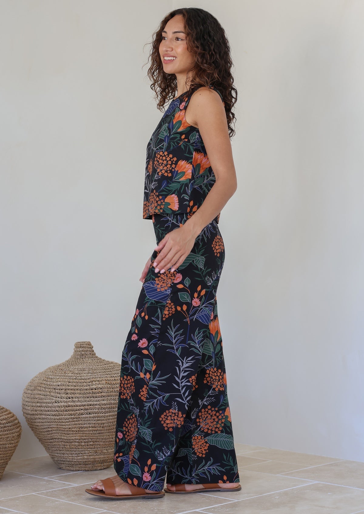 Model stands sideways wearing a 100% cotton high waisted wide leg pants in black based botanical print