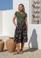 Woman wearing a knee length, box pleated cotton skirt with button front, belt loops and pockets in black based botanical print