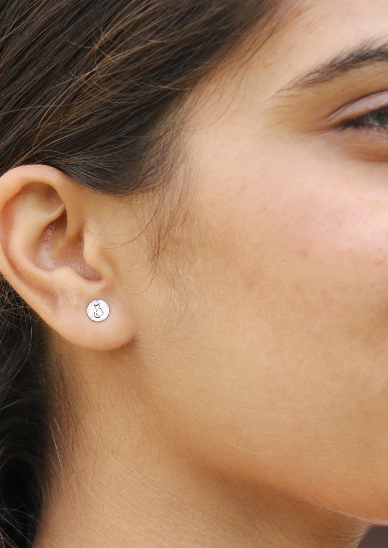 Close-up of a person wearing a small round studs with cat silhouette stamped into it 