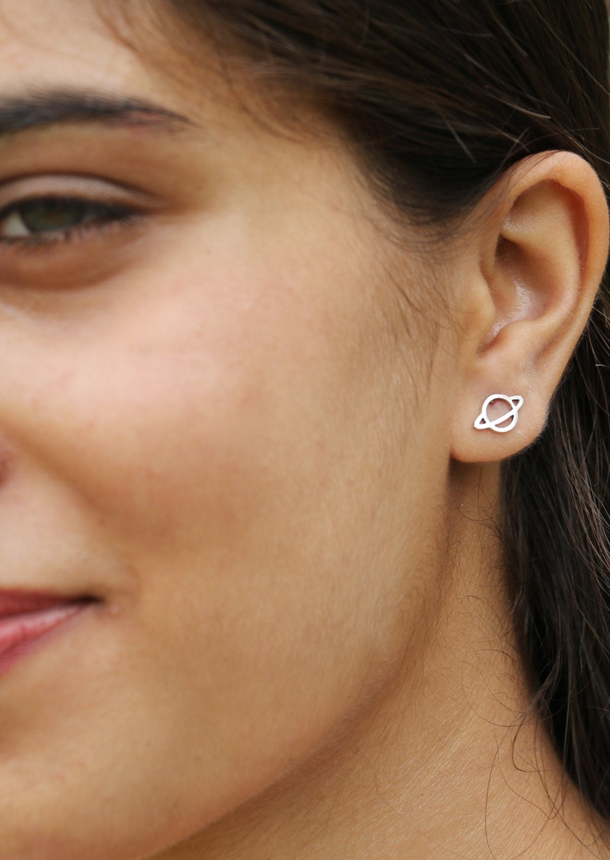 Close up of a woman wearing a silver saturn planet shaped studs with butterfly  backs