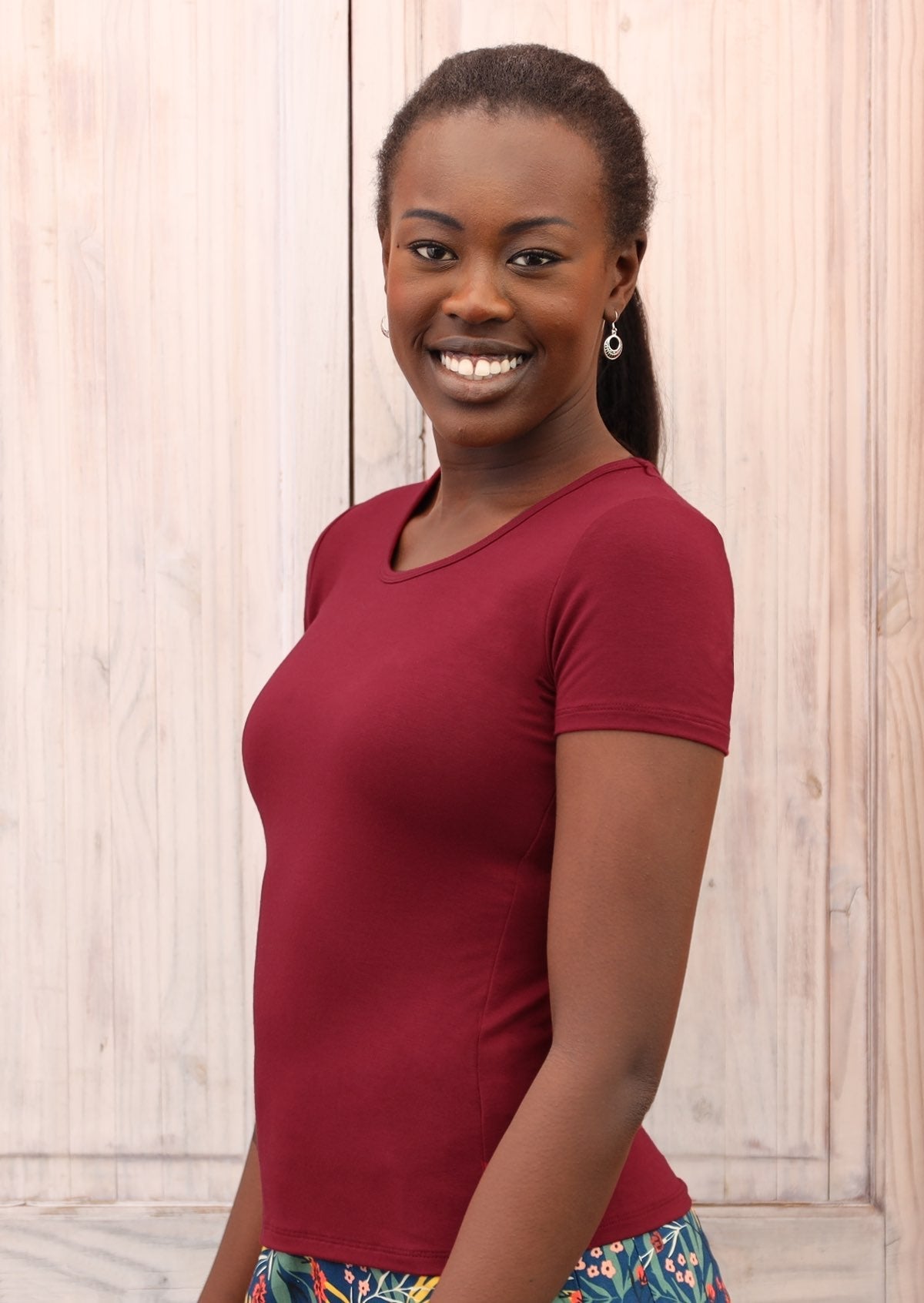 Woman with dark hair wearing a scoop neck maroon rayon fitted t-shirt.