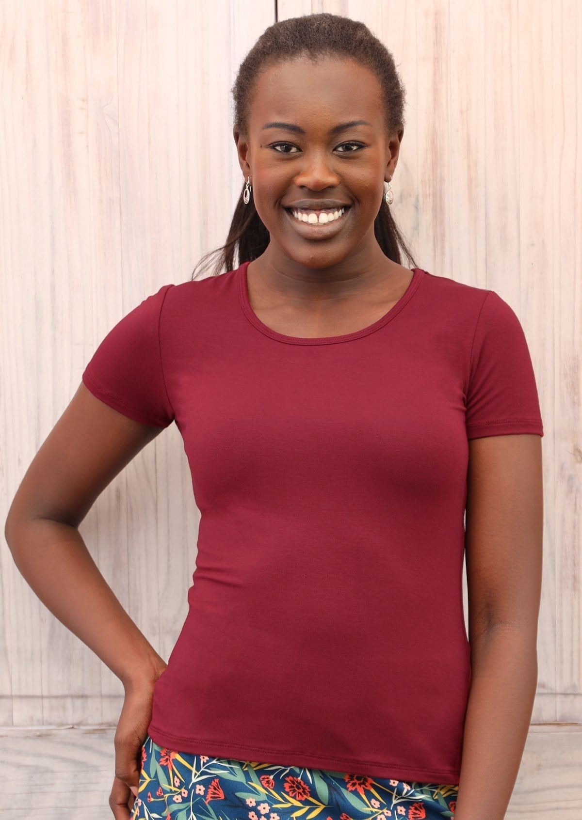 Woman with dark hair wearing a scoop neck maroon rayon fitted t-shirt with floral bottoms.