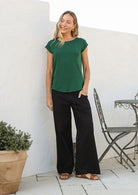 Woman wearing a 100% rayon forest green shell t-shirt with plain black pants in an outdoor setting