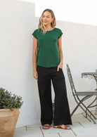 Woman wearing a 100% rayon forest green shell t-shirt standing against a white wall.