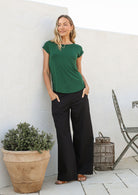 Woman leans on wall wearing a 100% rayon forest green shell t-shirt and plain pants