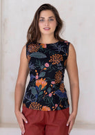 Woman wearing a sleeveless top with a black based floral print, paired with rust coloured pants 
