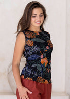 Woman standing side on wearing a black sleeveless top with floral patterns against a neutral background