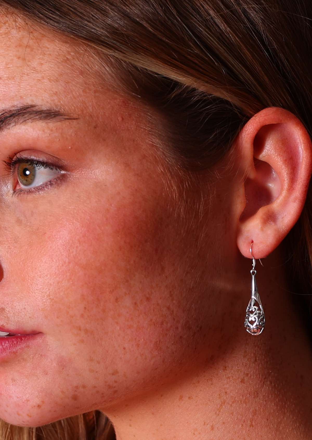 Woman wears silver teardrop shape filigree cutout detailed earrings, suspended from wire hooks