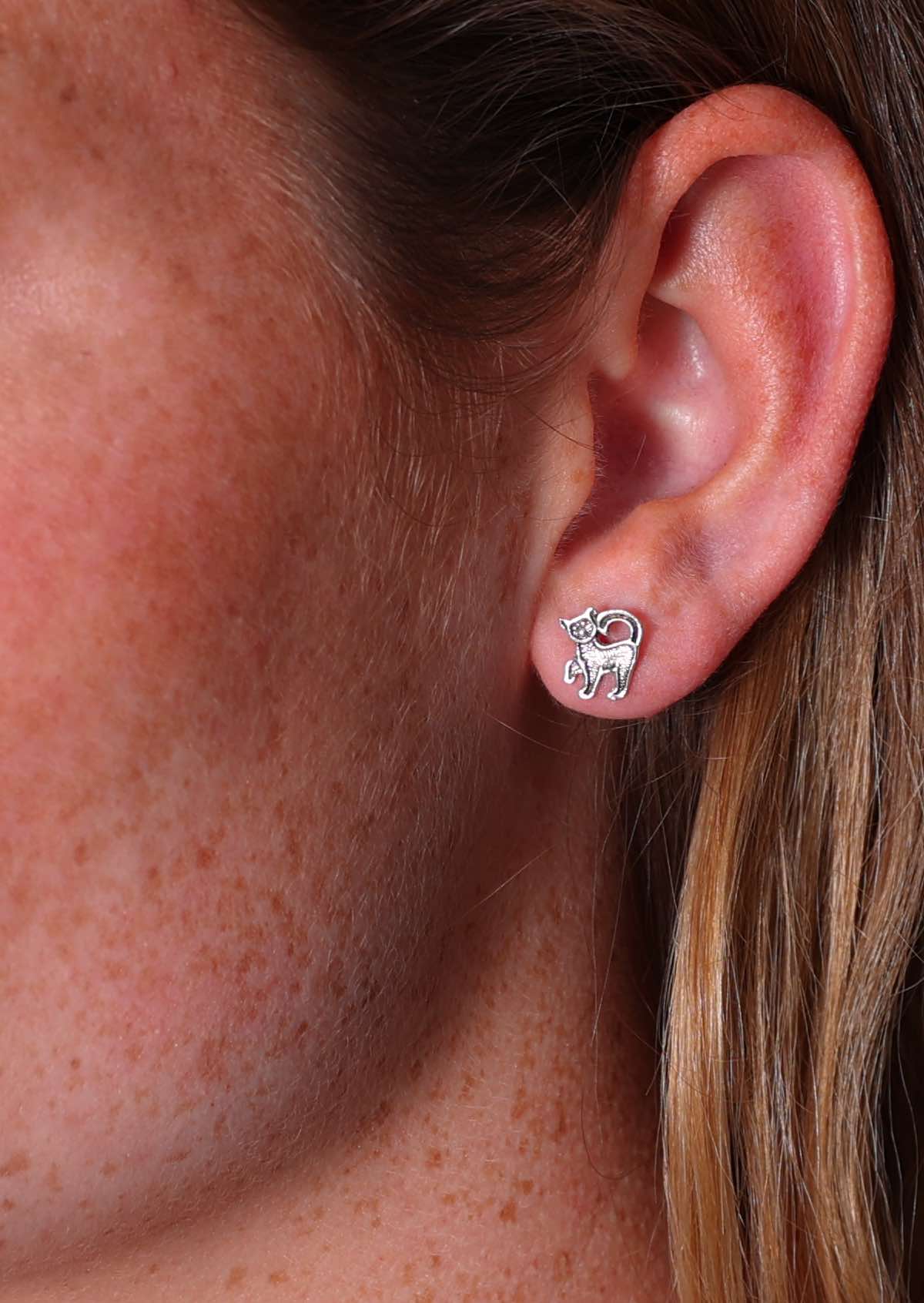 A close-up image of a person wearing sterling silver kitten stud earrings in the shape of a cat.