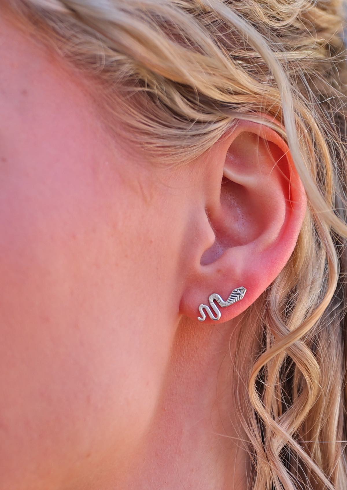 close up of woman's ear wearing silver snake stud earring with a flowing, curvy shape.