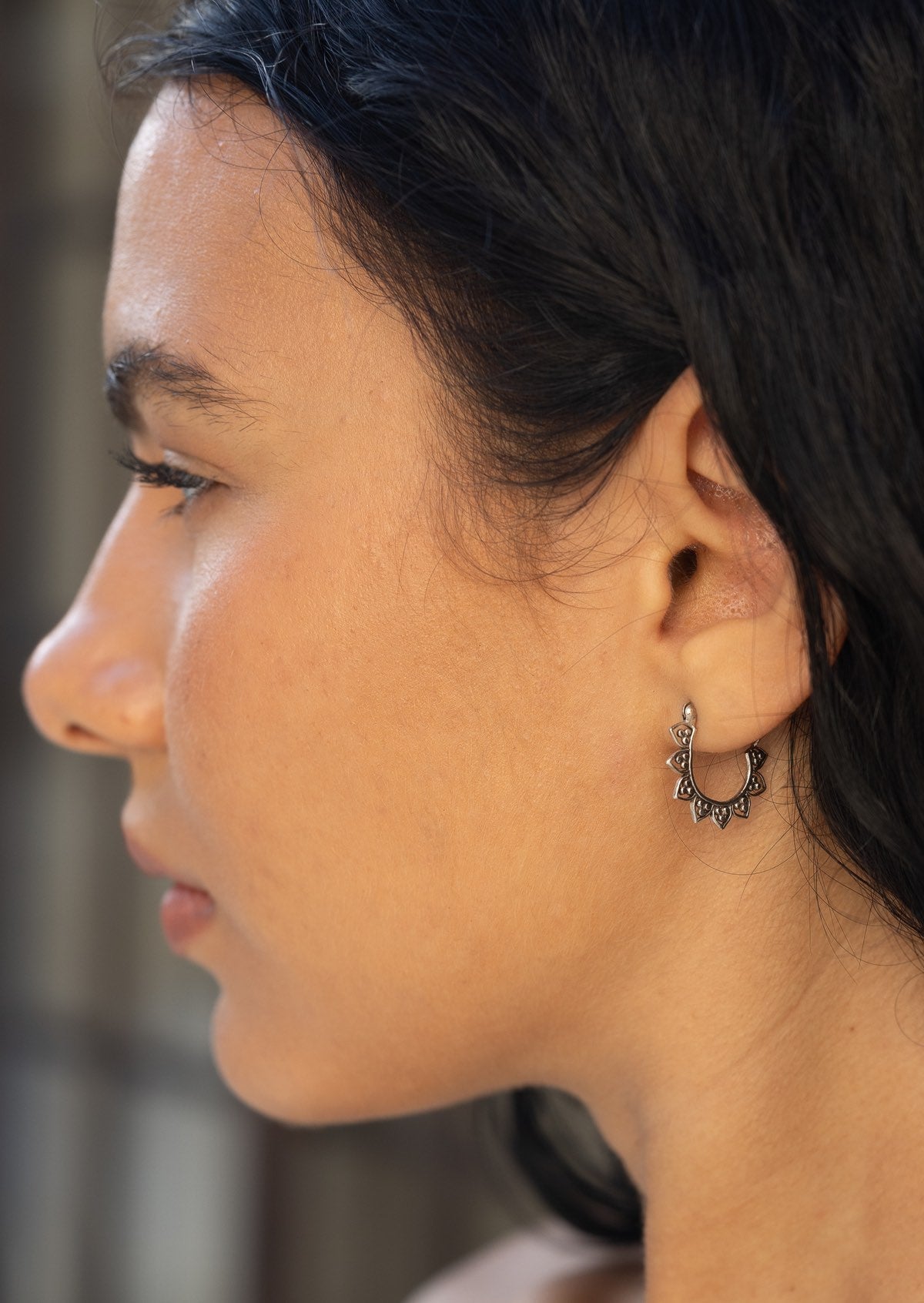 Close-up of a woman wearing a sterling silver hoop earring with flower petals around the outer edge