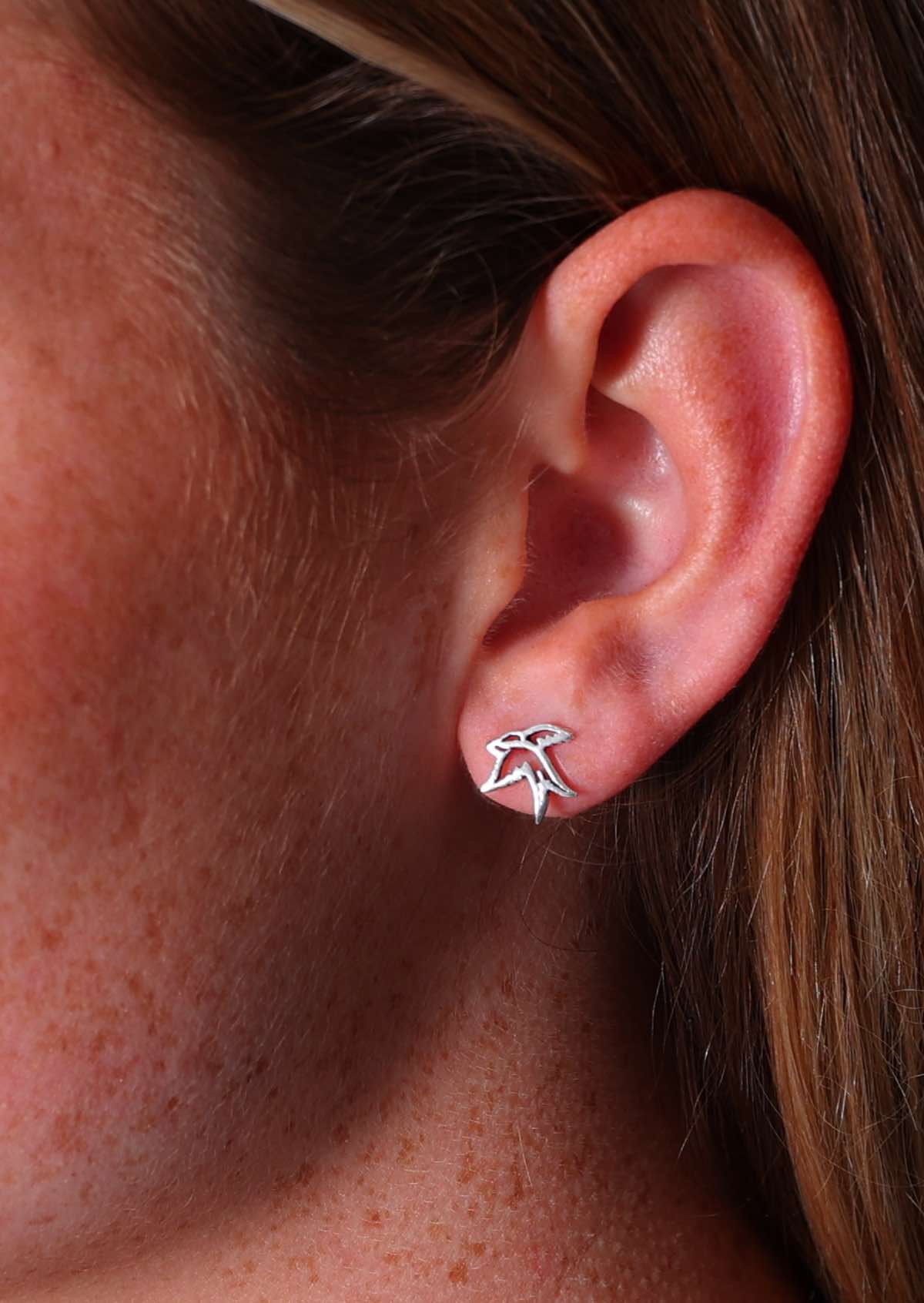 A close-up image of a person wearing a silver Swallow stud earring in the shape of a swallow bird.