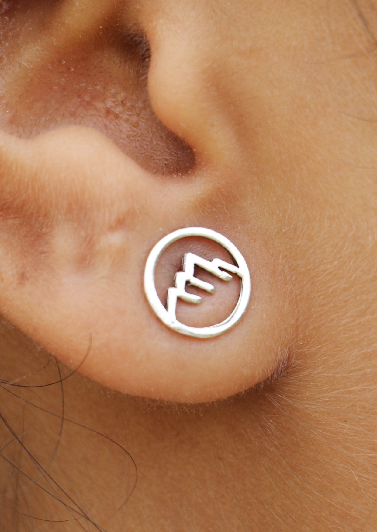 Close up of a sterling silver circular Alps studs with delicate mountain cutout details 