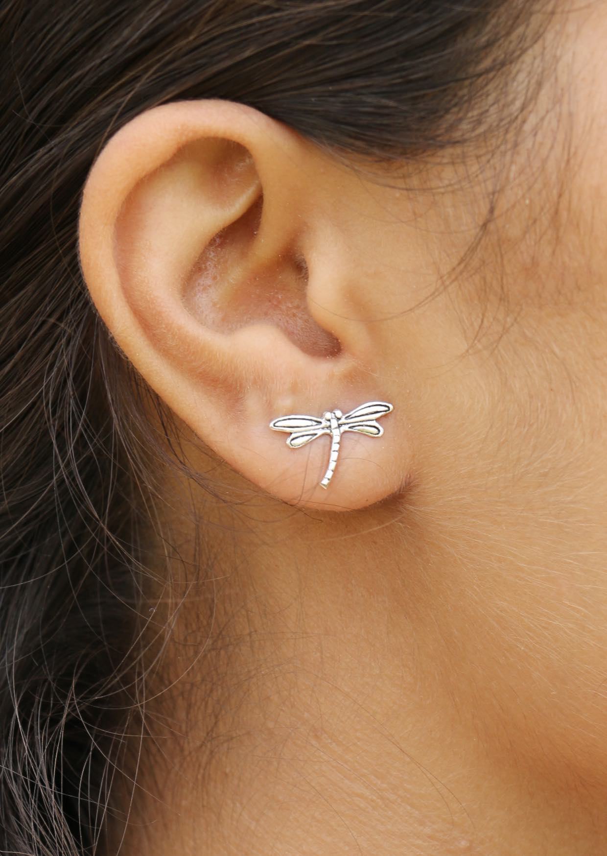 Silver dragonfly studs with intricate wing cutout, worn by a woman with dark hairs 