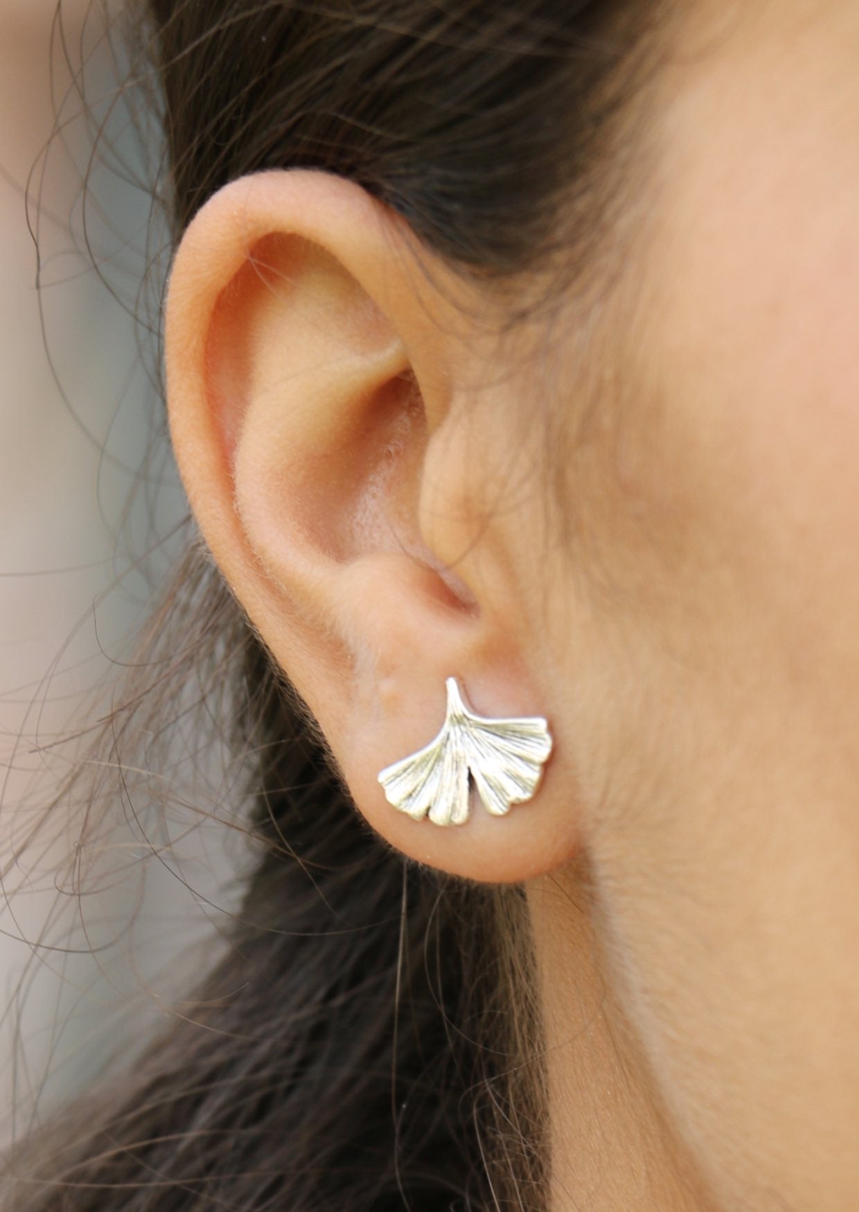 Woman wearing delicate sterling silver Ginkgo Studs featuring fan-shaped leaves with subtle veined texture