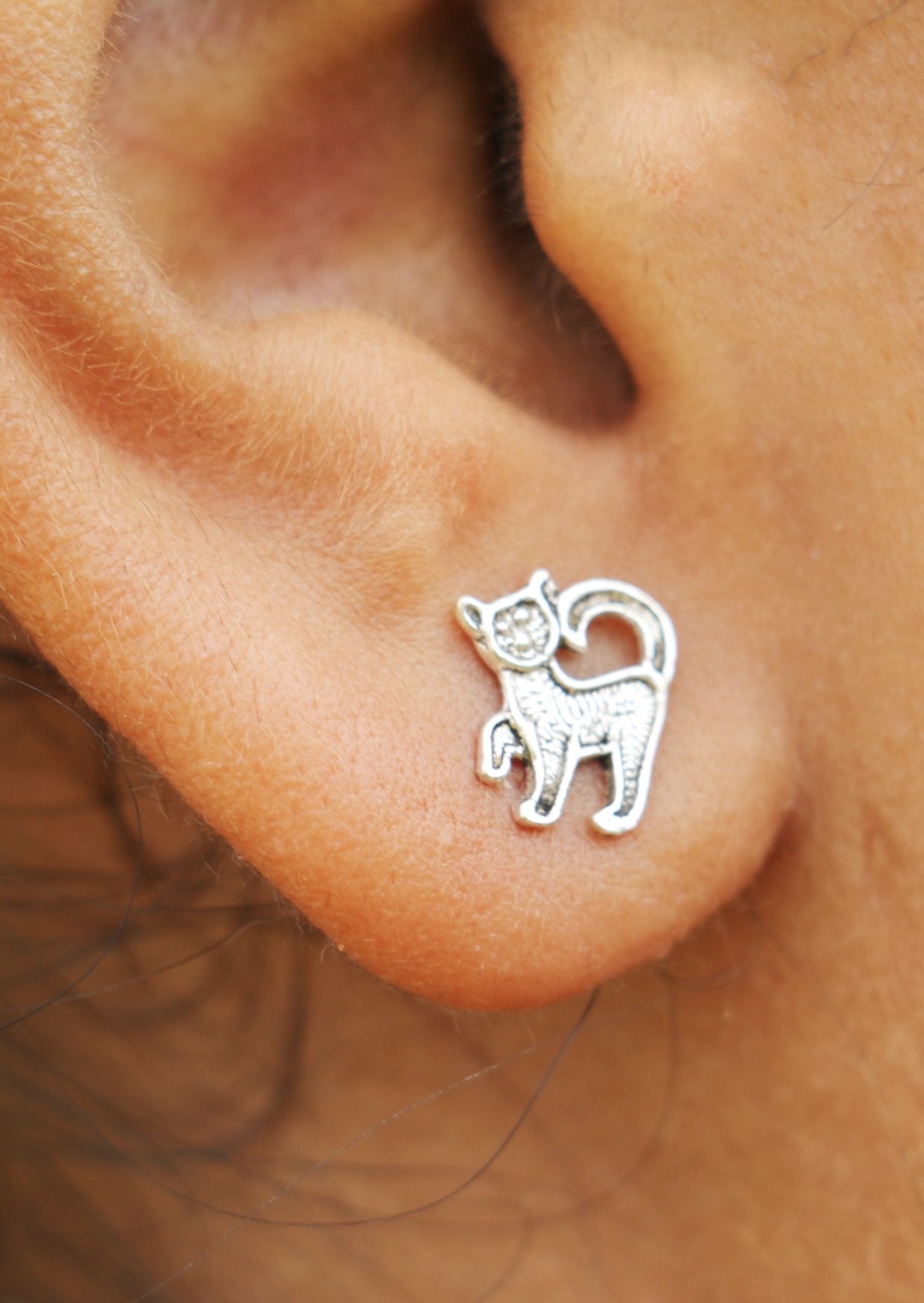 Close up of a sterling silver kitten studs featuring feline design and secure butterfly backs 
