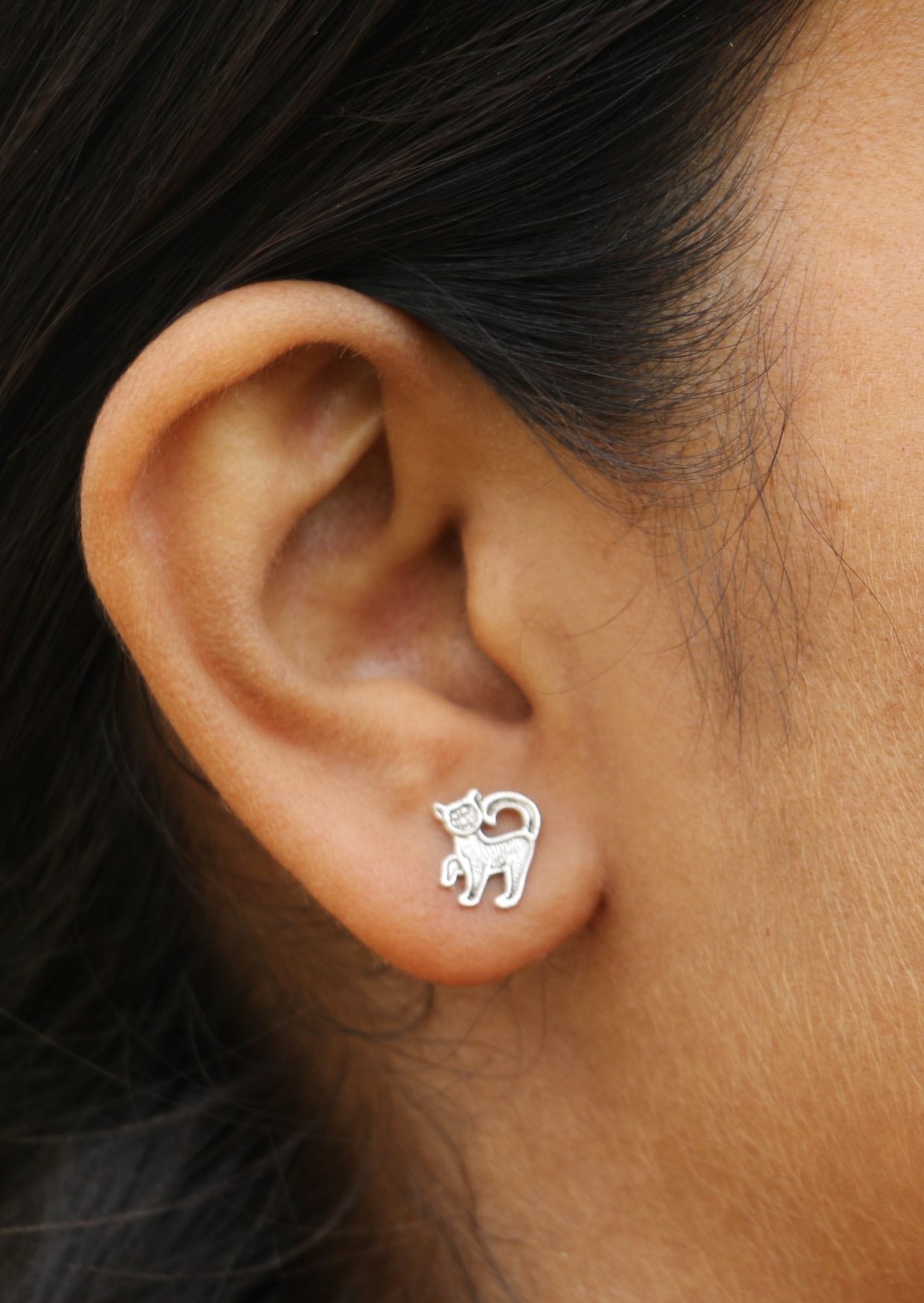 Close-up of a woman with black hair wearing silver cat-shaped studs with butterfly backs