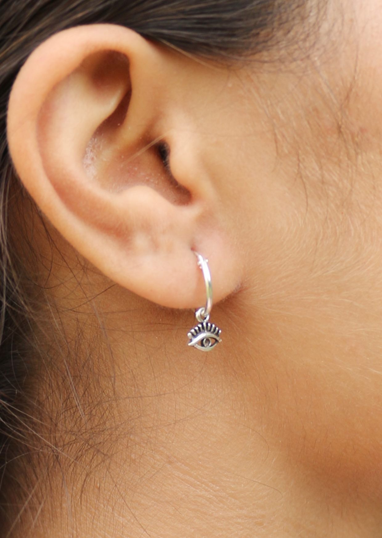 Close-up of an ear wearing a silver hoop earring with a small eye charm 