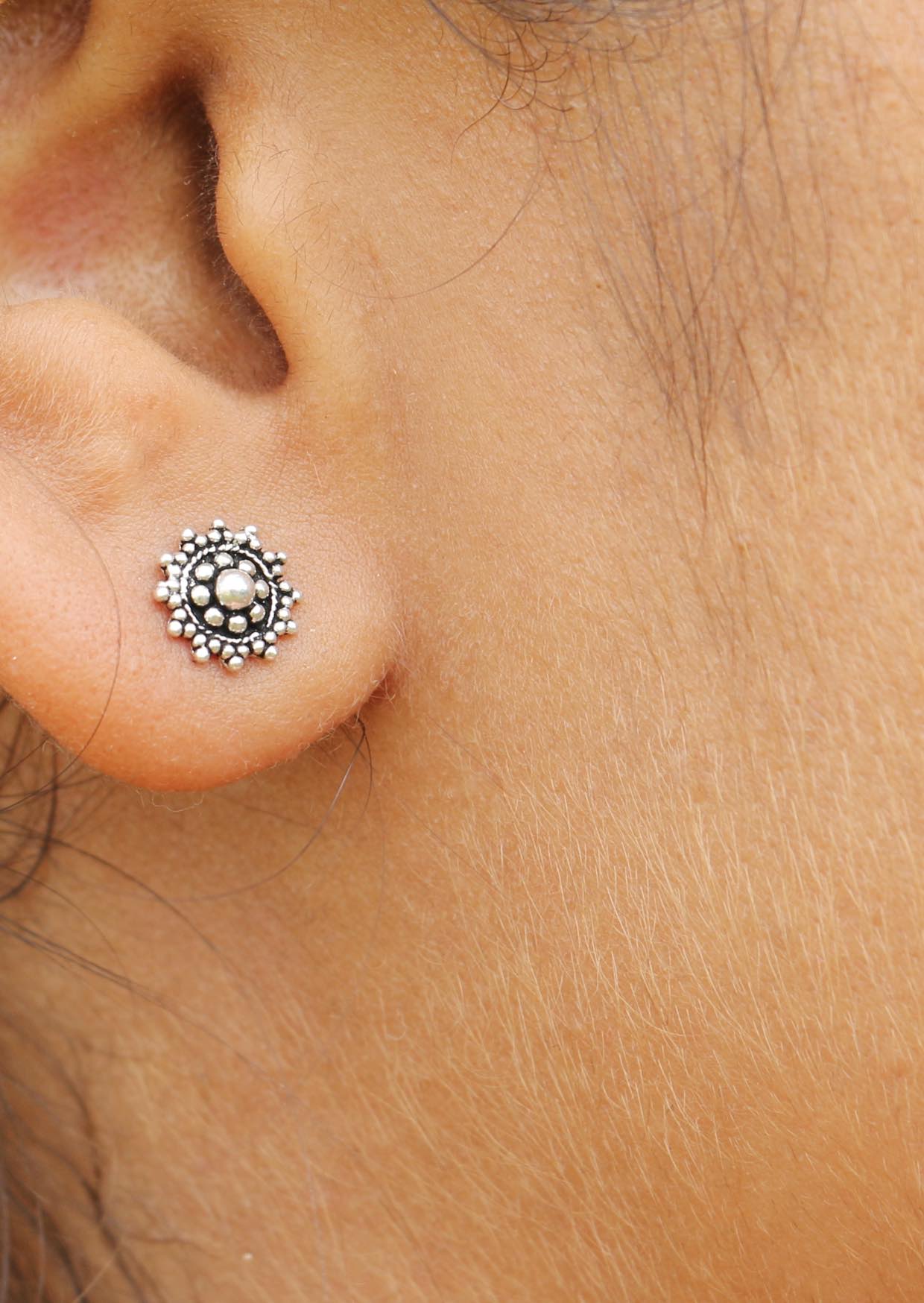 Close-up of an ear with a silver ornate stud earrings with beautiful intricate design 