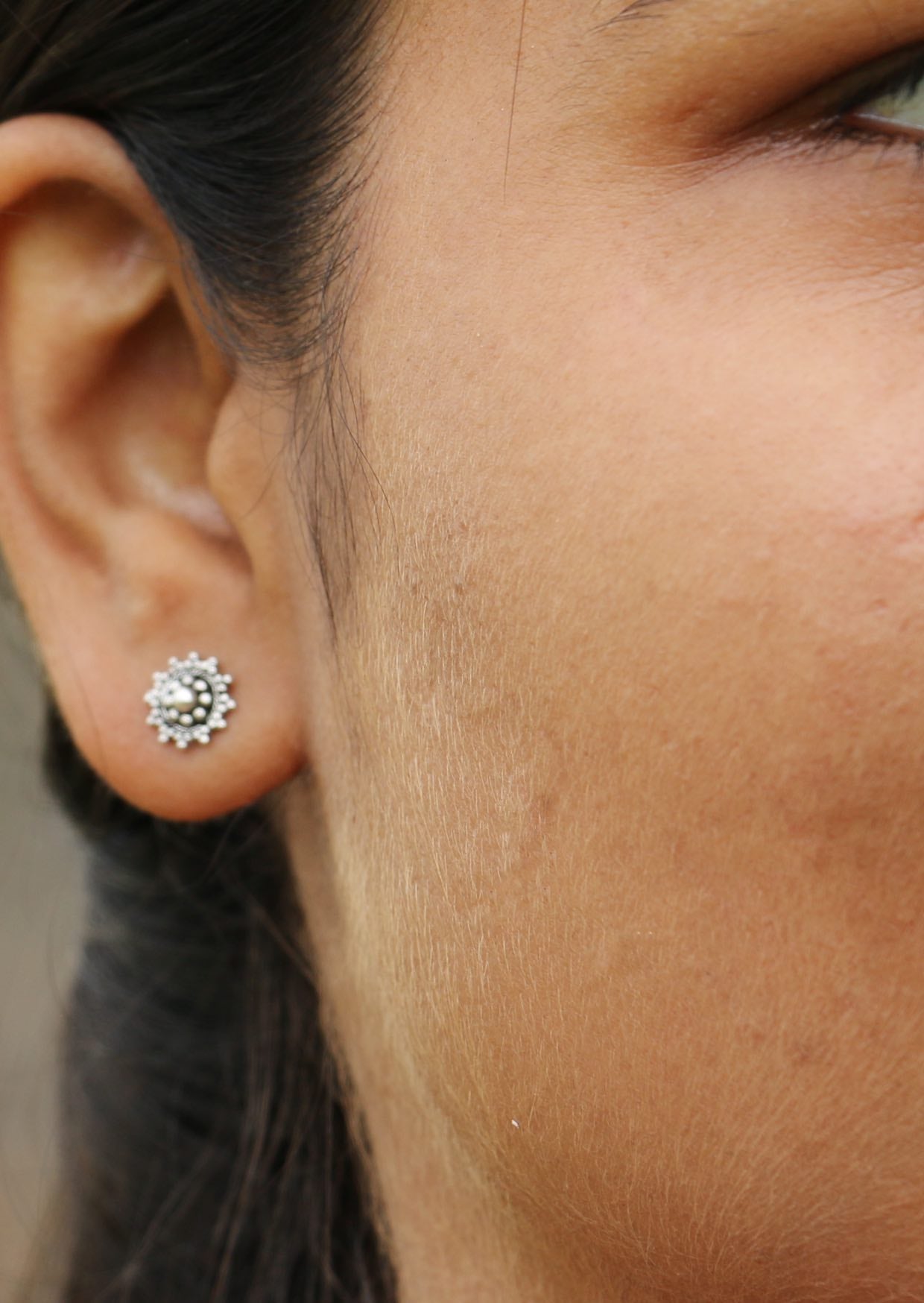 Silver circular studs featuring an intricate ornate design with butterfly backs, worn on a woman’s ear