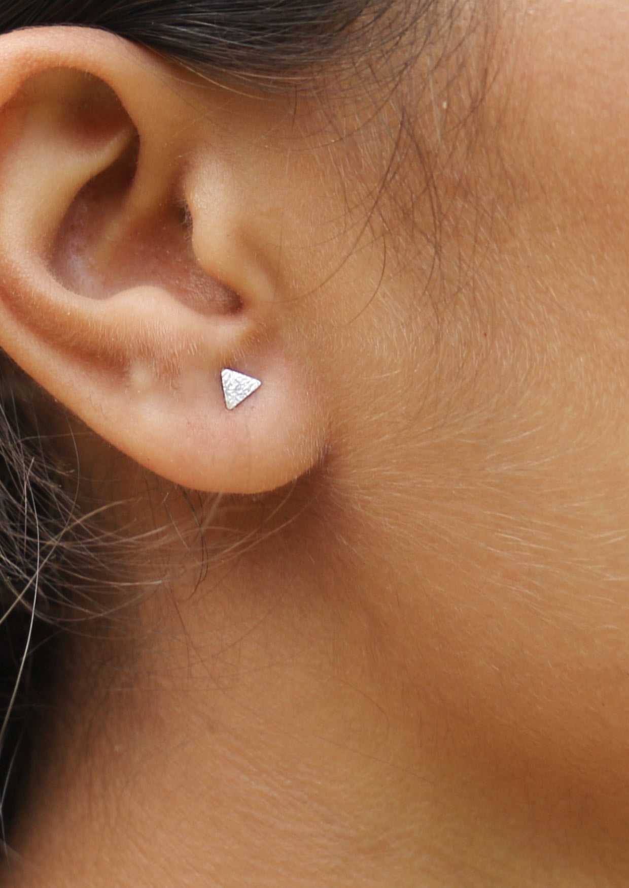 Silver triangle stud earrings with a textured design, displayed on a woman's ear 