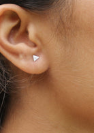 Silver triangle stud earrings with a textured design, displayed on a woman's ear 