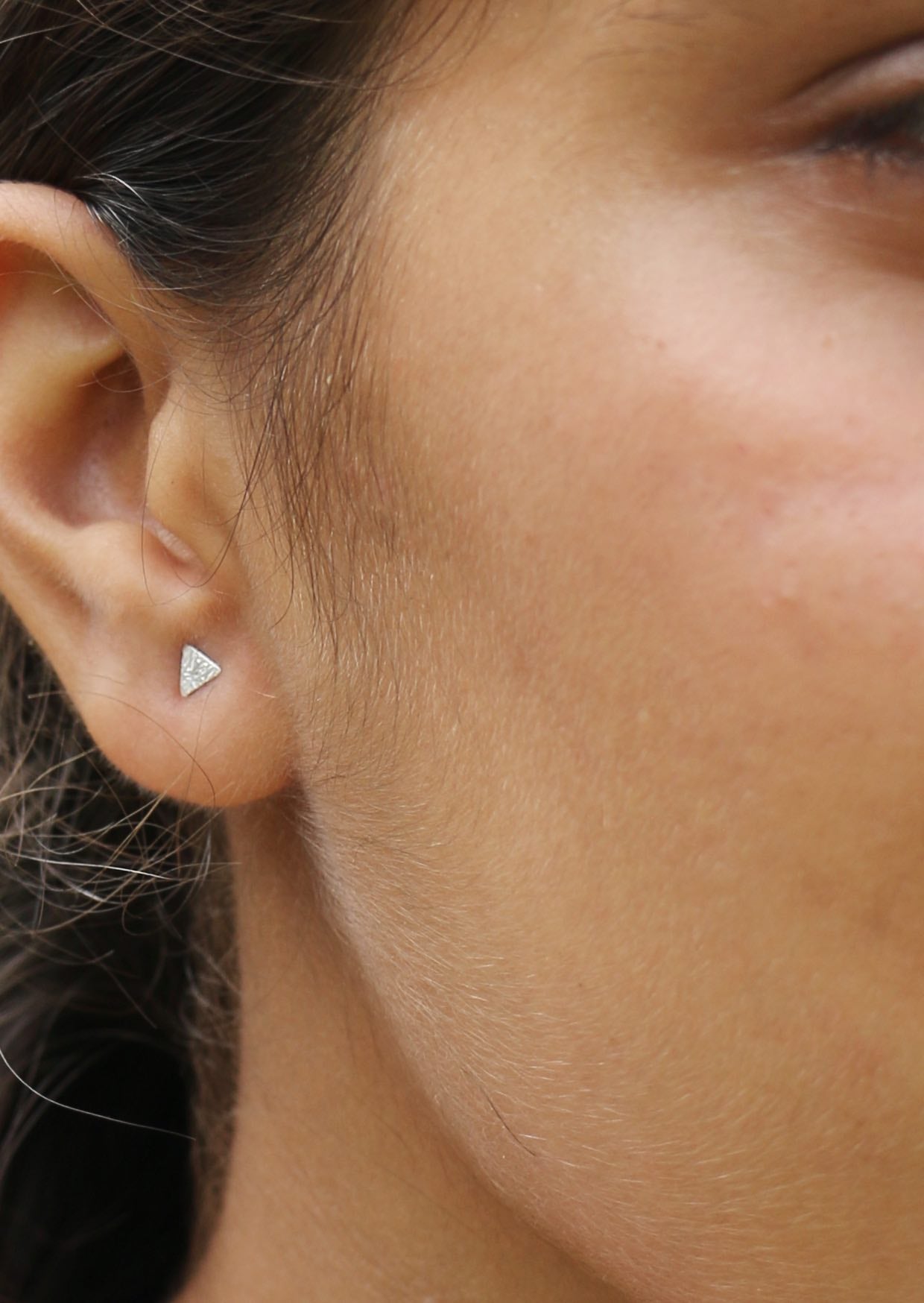 Close-up of an ear wearing a triangle-shaped studs with a textured design and secure butterfly backs 