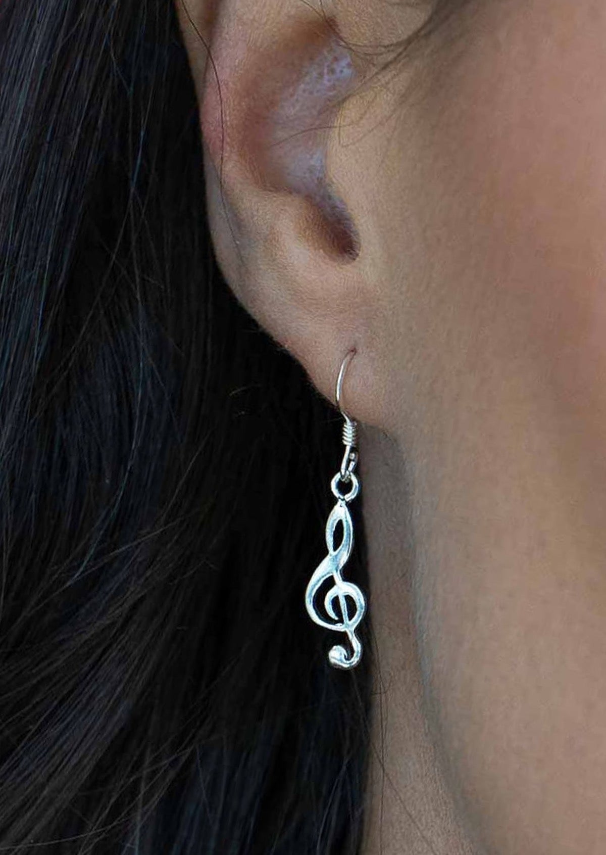 woman's ear wearing dangly silver treble cleft music earring 
