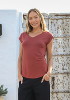 Woman wearing a 100% rayon terracotta V-neck T-shirt and black pants, standing against a wall.
