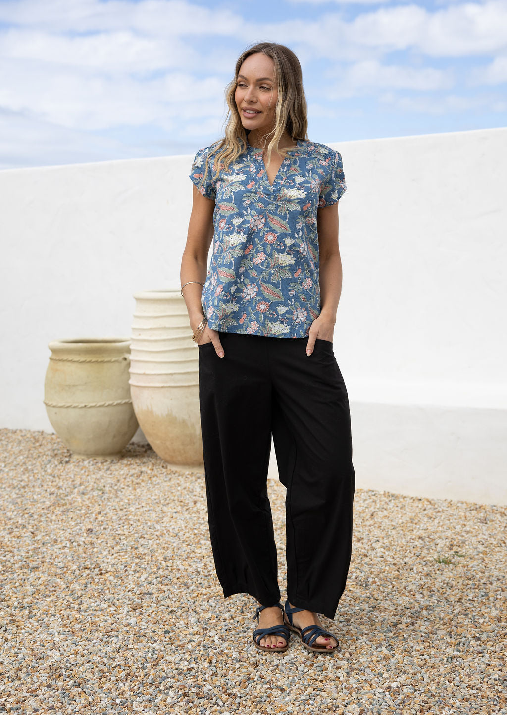Woman wears a loose fit floral cotton top in dusty blue with short sleeve, mandarin collar and V neckline.