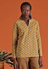 Model wearing mustard coloured long sleeve women's top with open collar and tan cotton pants