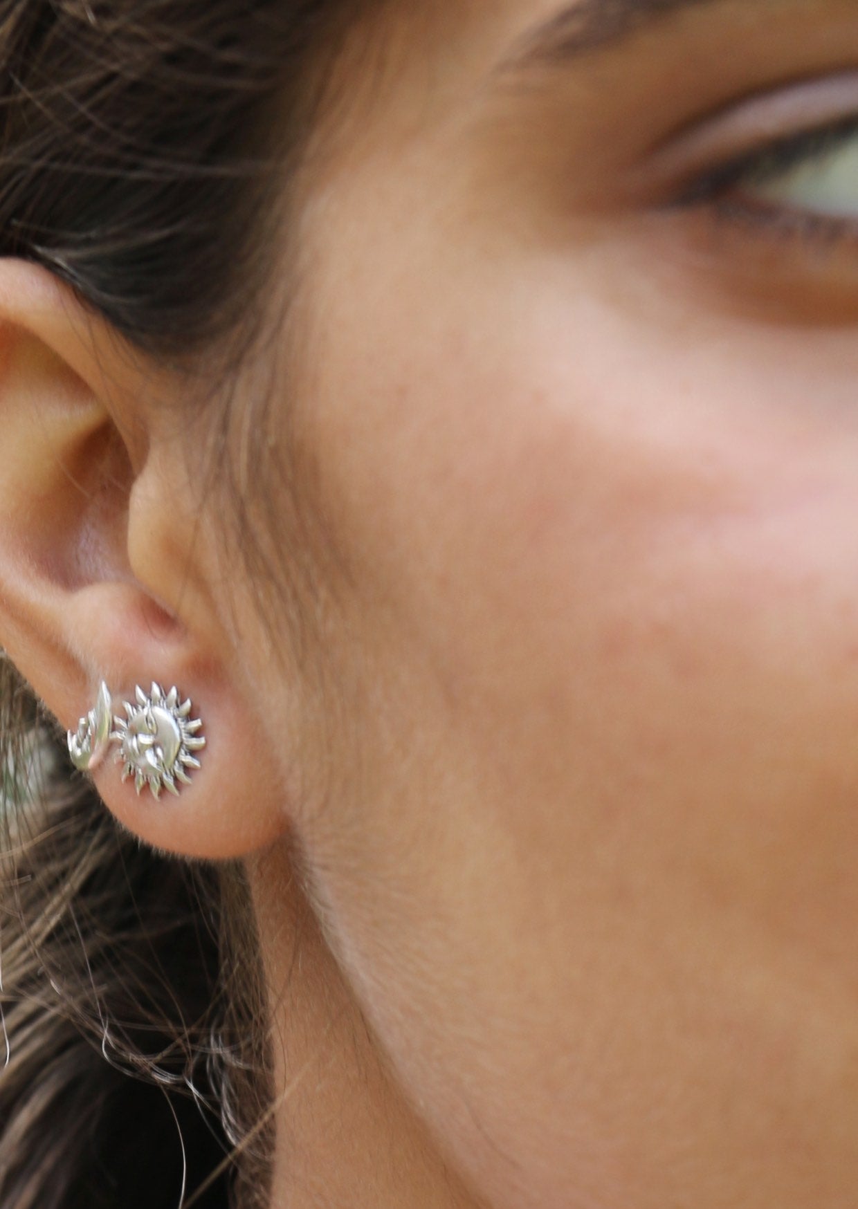 Close-up of an ear wearing a silver sun and moon shaped studs with subtle carved faces