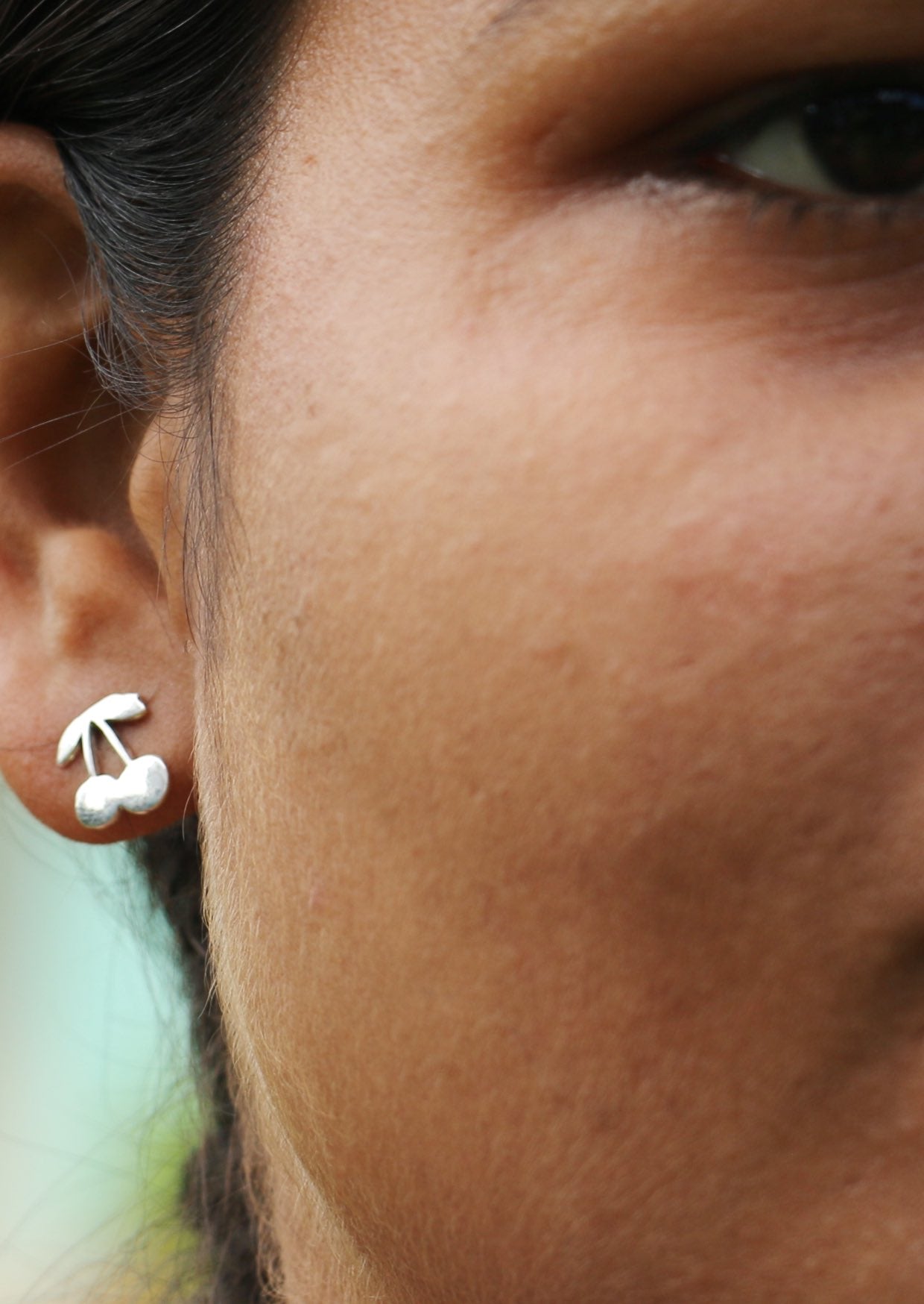 Woman with black eyes is wearing sweet cherry sterling silver studs with secure butterfly backs