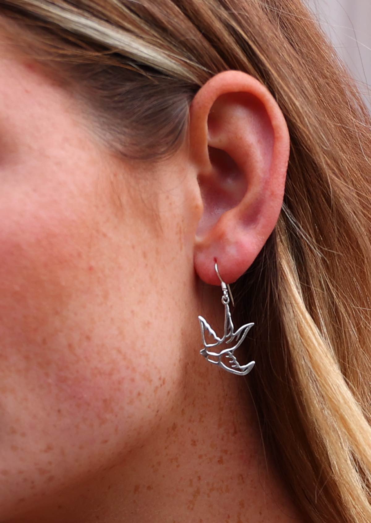 Woman wearing dangly silver hook style bird earrings 