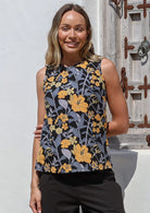 Woman wearing a sleeveless 100% cotton top with round neckline in black based retro - yellow and grey floral print
