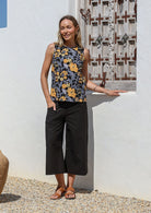 Woman standing in sun wearing black cotton pants paired with sleeveless floral cotton top with high round neckline
