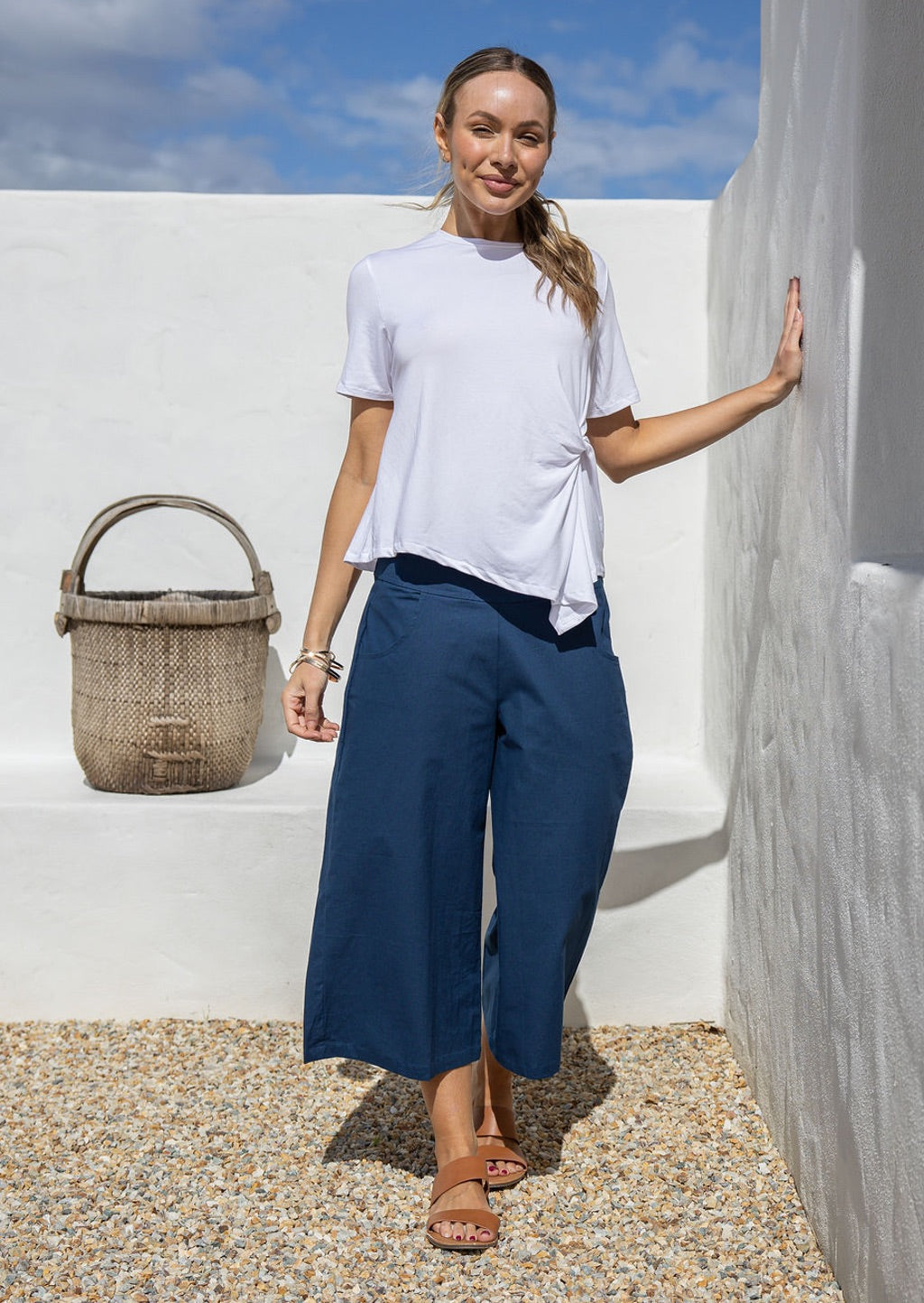 Woman stands in 100% cotton wide leg 3/4 pants in dark sea blue paired with a white rayon basic top 