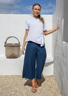 Woman stands in 100% cotton wide leg 3/4 pants in dark sea blue paired with a white rayon basic top 