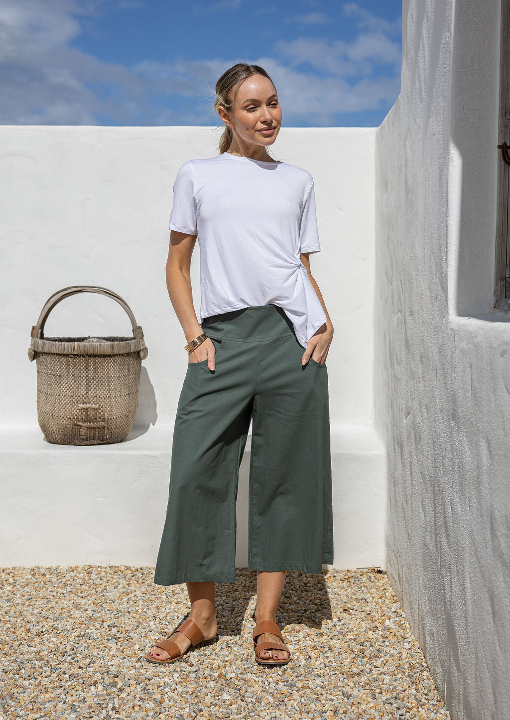 Woman wears 3/4 length wide-leg cotton pants in jungle green shade with her hands in pockets 