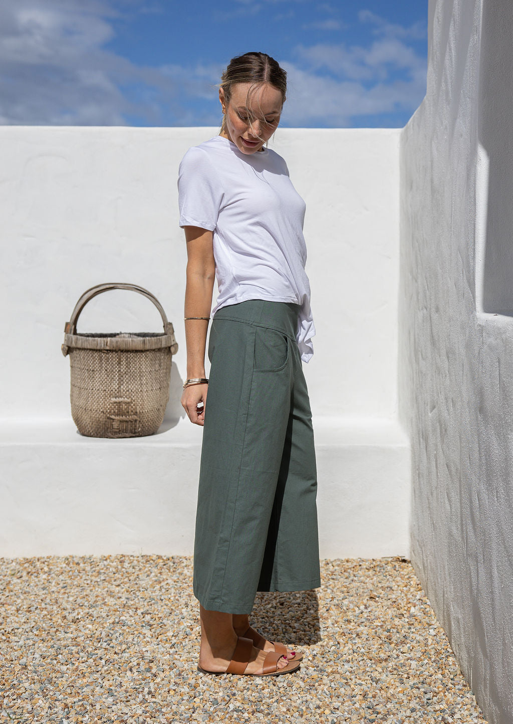 Woman stands against the white background in green wide leg cotton pants with pockets, side zipper and 3/4 length